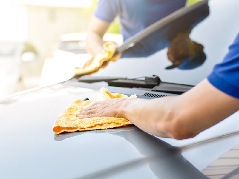 Person cleaning a car hood with a cloth