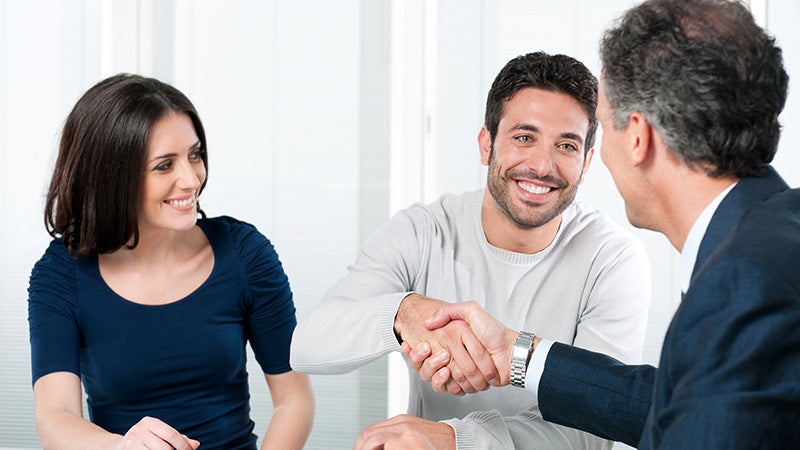 Smiling couple shaking hands with car dealer during consultation